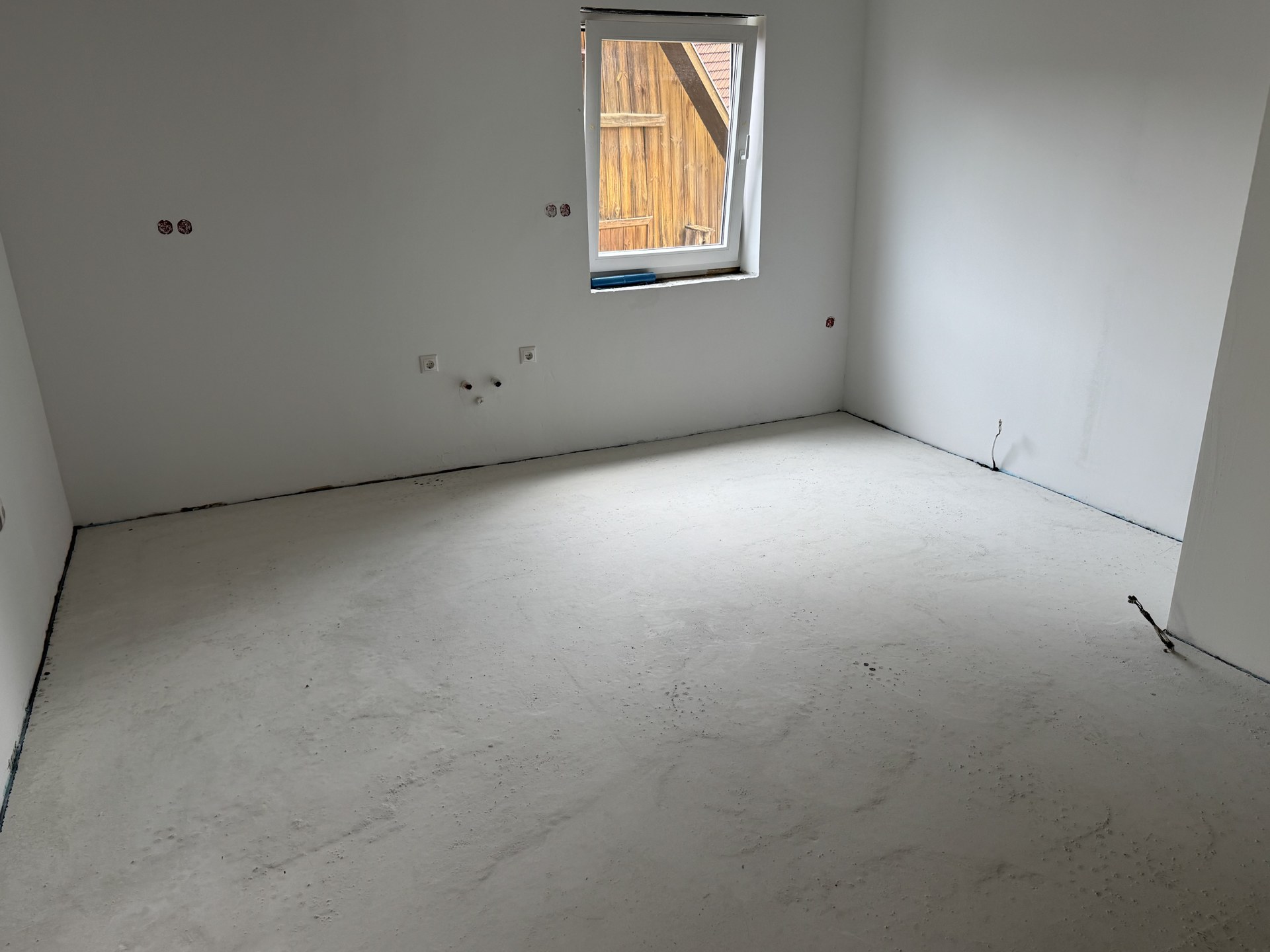 Leerer Raum im Dachgeschoss mit fertig begradigtem Estrich vor Beginn der Fliesenarbeiten