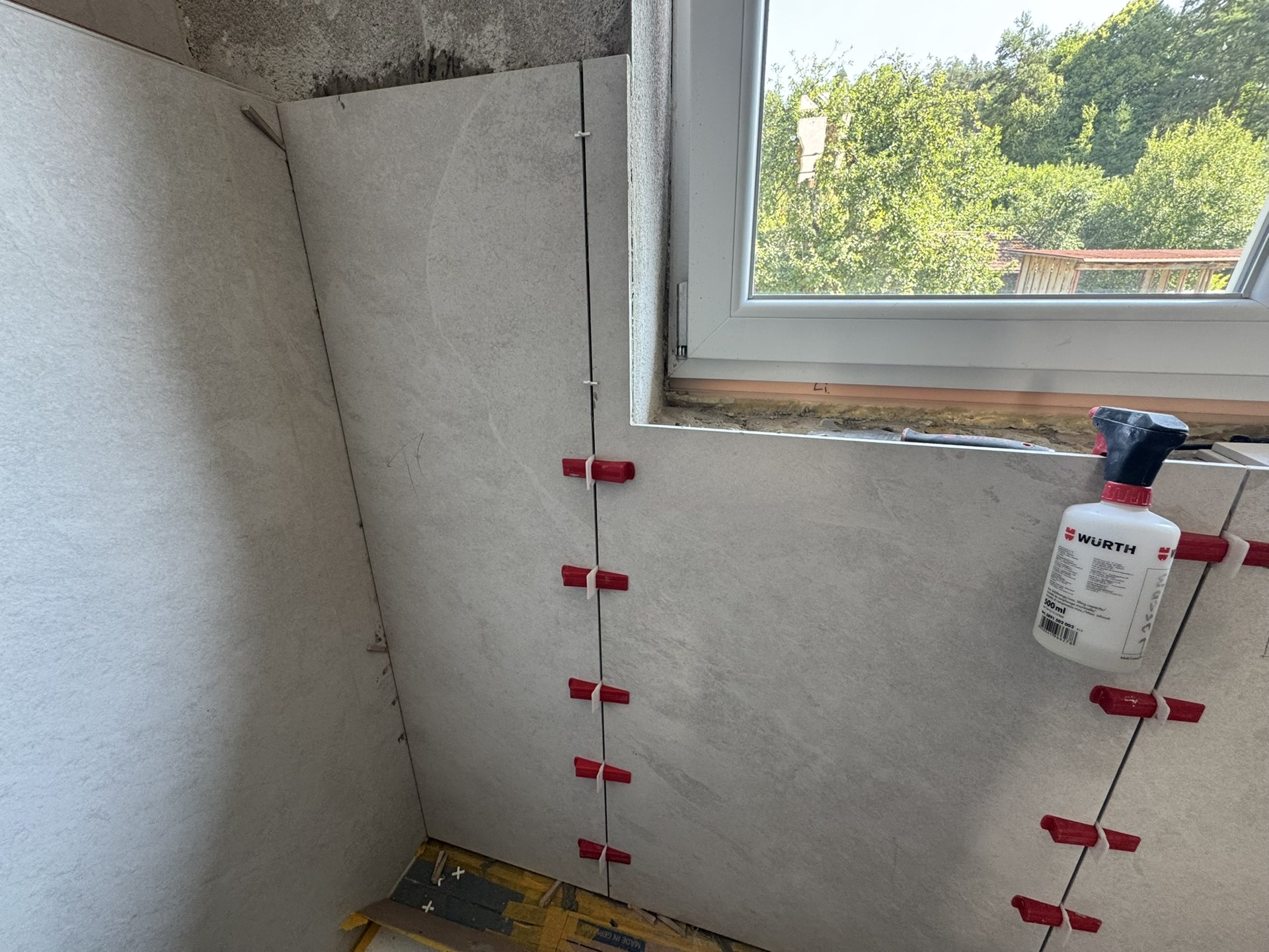 Wandfliesen laufen auf die Fensterlaibung zu, ausgerichtet mit Nivellierklammern