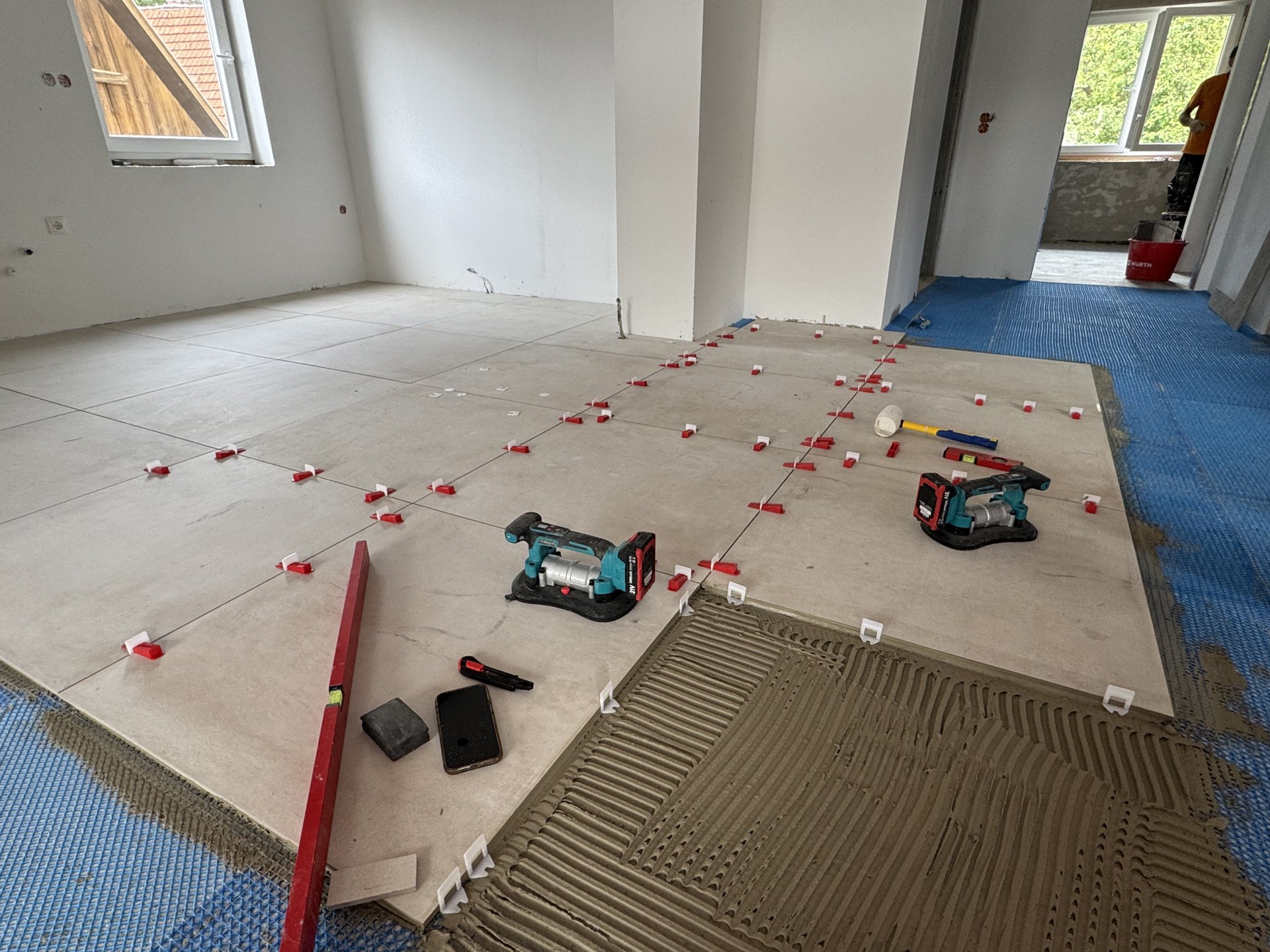 Großformatige Bodenfliesen mit Nivelliersystem, aufgekämmtes Kleberbett und Werkzeug auf der Verlegefläche
